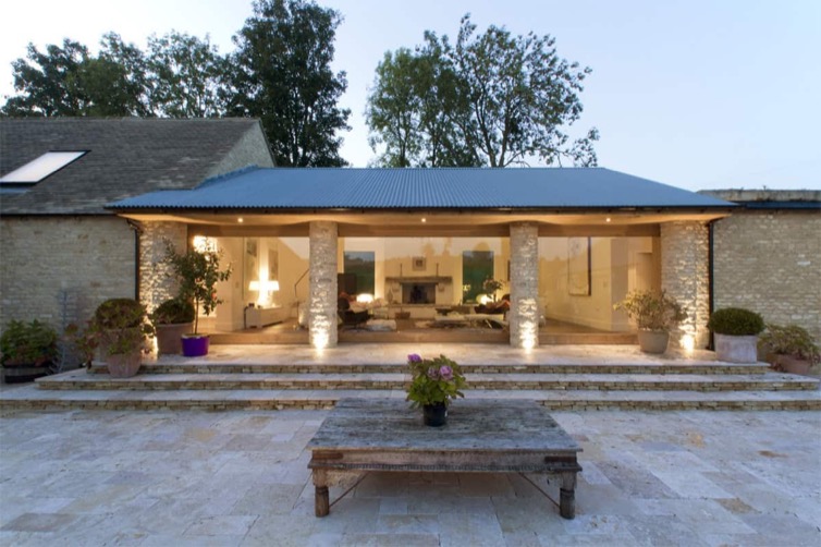Vale Farm converted barn at dusk with full-height glazing, stone columns and lit living room interior